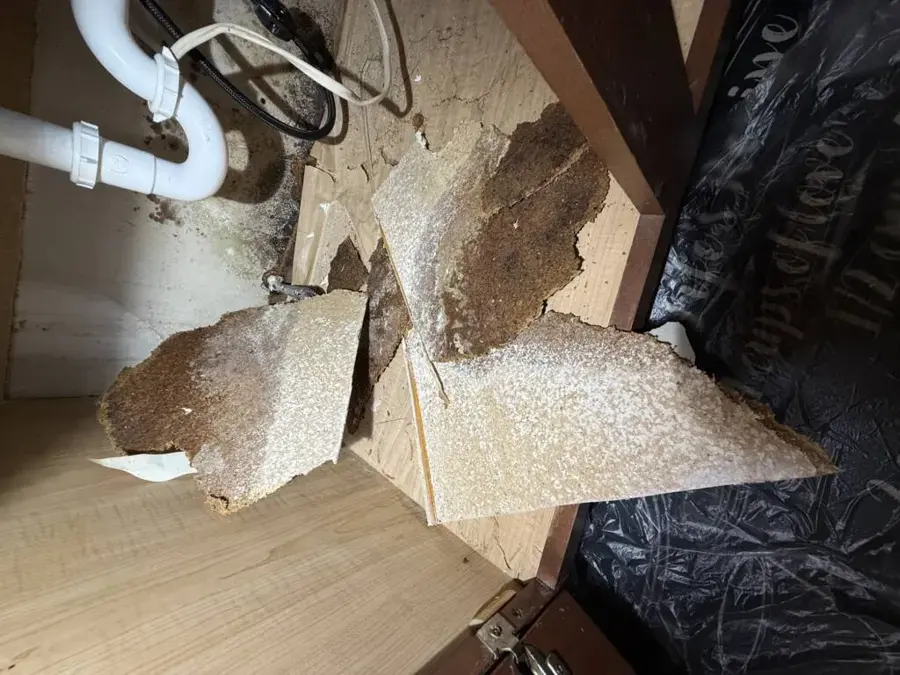 Broken, swollen sink cabinet floor pulled apart after a slow leak