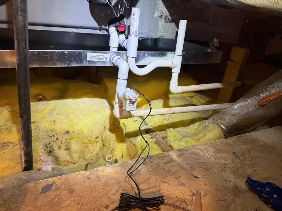 Attic air handler drain pipes above wet insulation where condensate overflowed
