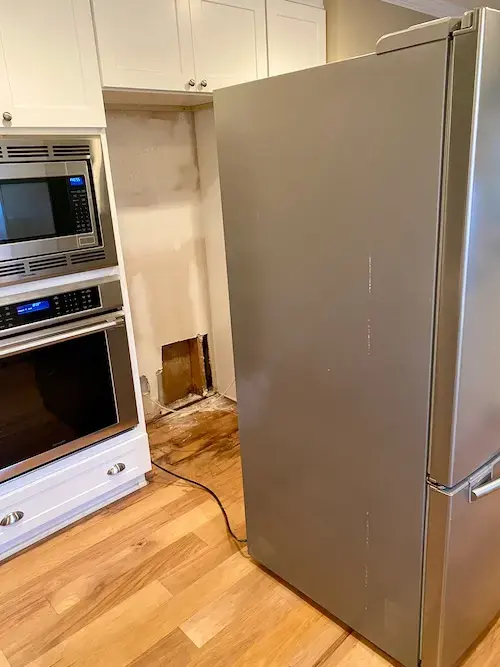 Refrigerator pulled out from the cabinets with wet hardwood flooring around it