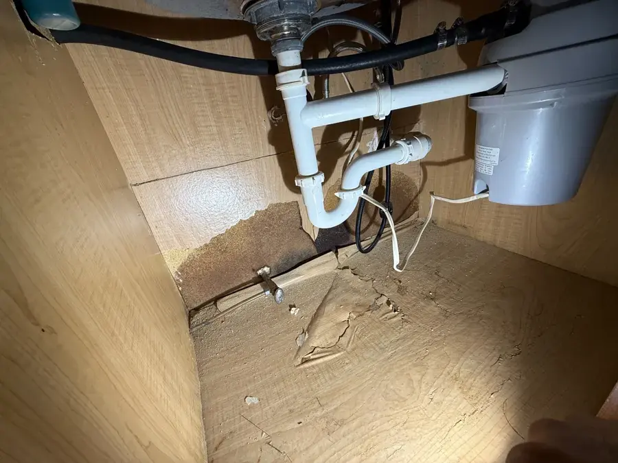 Swollen, water-stained sink cabinet floor under a leaking drain and supply pipe