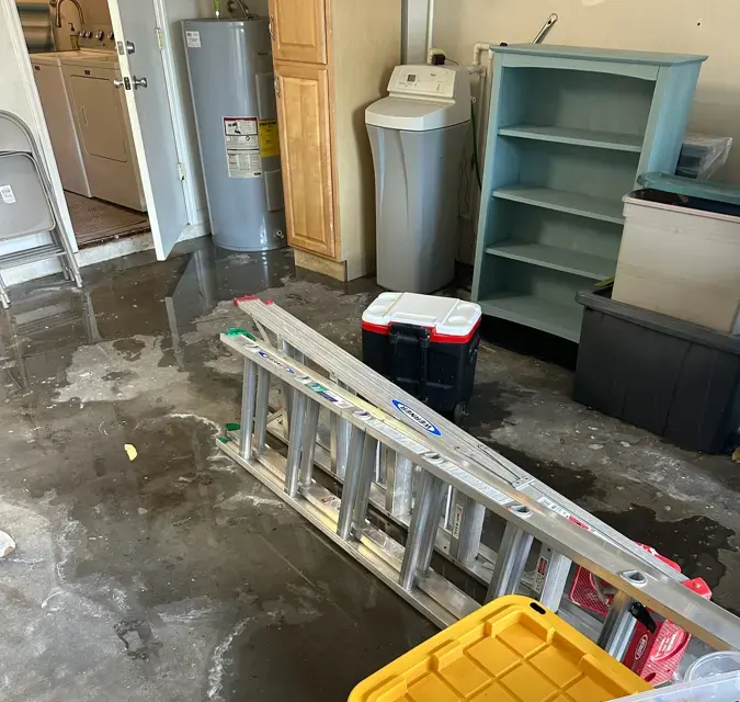 Water spread across a garage floor around a ladder, storage bins and shelves